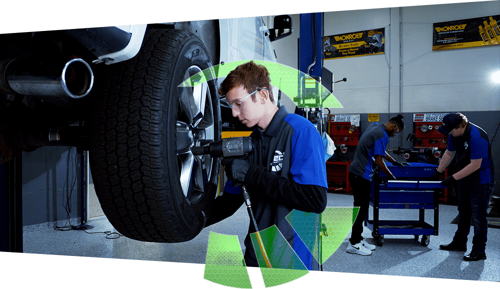 Photo of a J-Tech Automotive Technology student working hands-on with an impact wrench to change a tire on a car on a lift in the Automotive Technology lab.