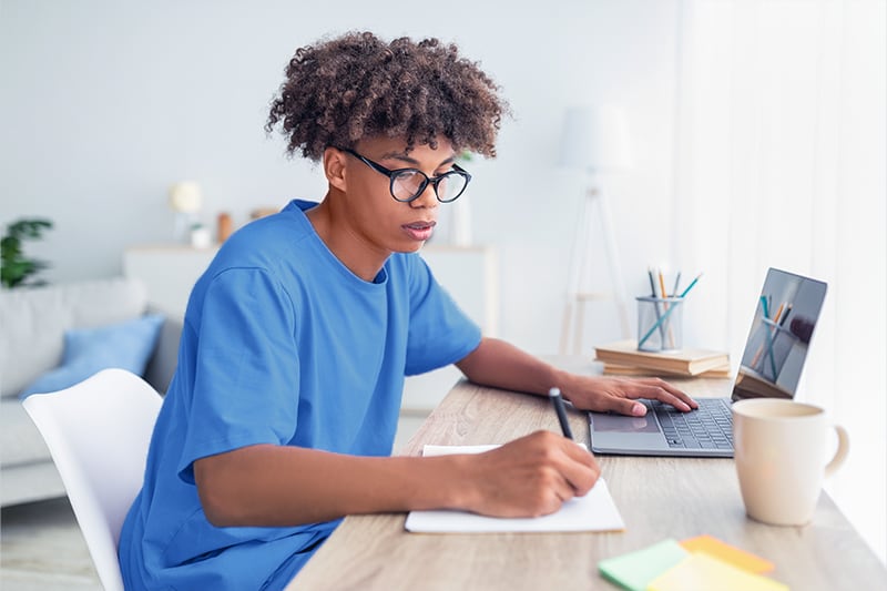 Photo of a young man applying for financial aid on a laptop at home.