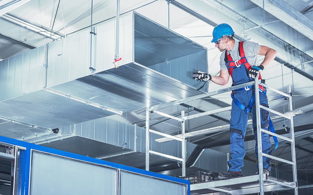 Commercial HVAC installer inspecting the massive ducts in the ceiling.