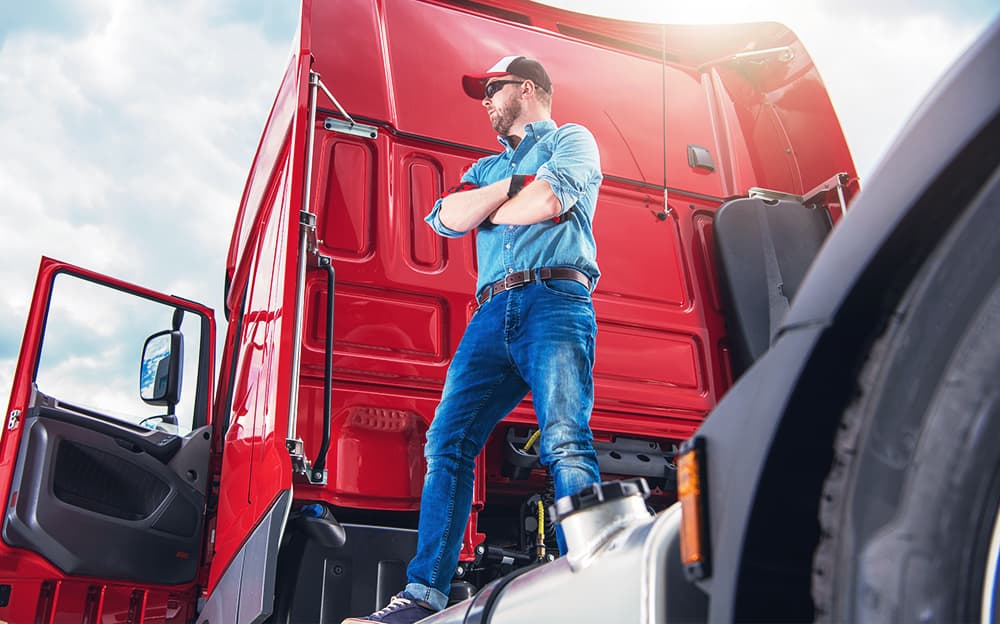 A truck driver standing behind his tractor.