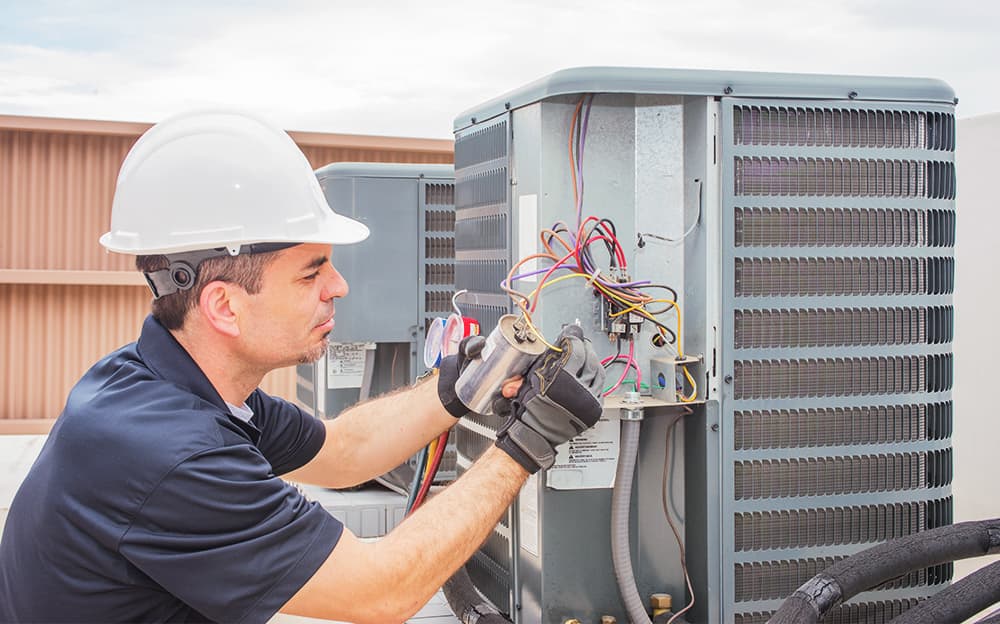 HVAC maintenance technician inspecting the wiring on an industrial AC unit.