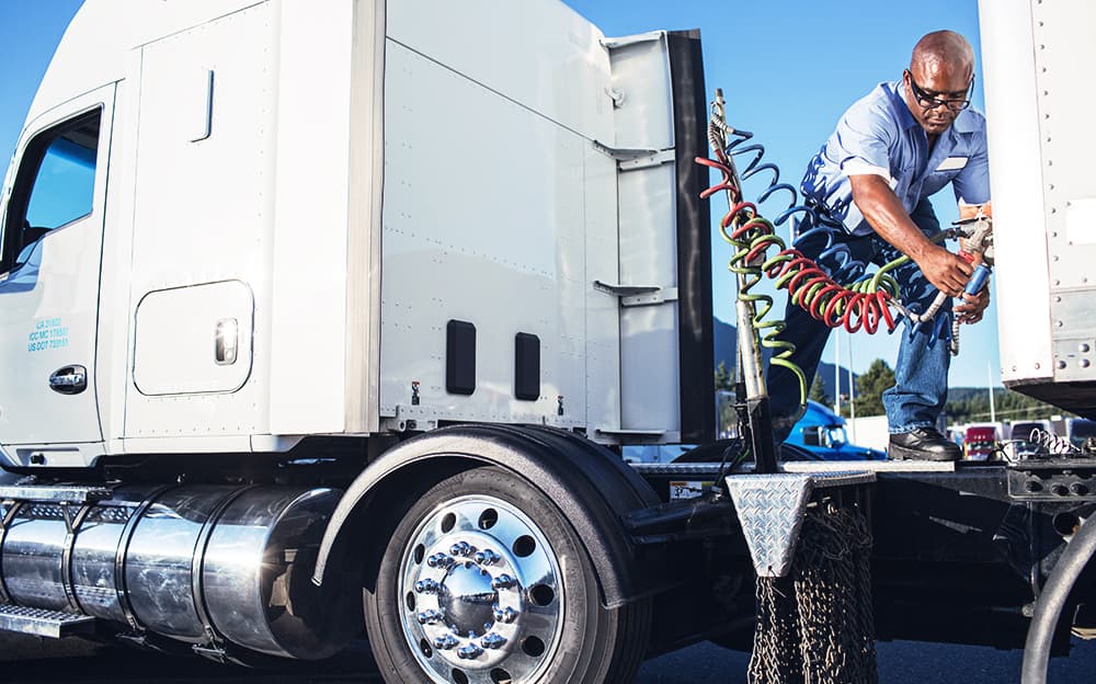 An African-American truck driver attaching power cables from his tractor to his trailer at a truck stop.