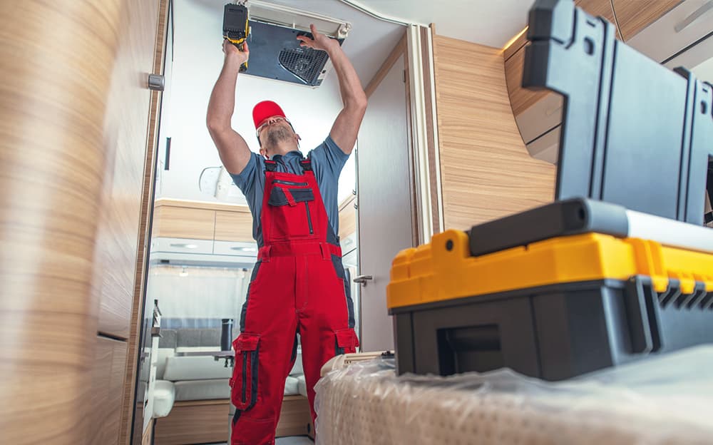 RV technician fixing the ceiling-mounted air conditioner in a motorhome.