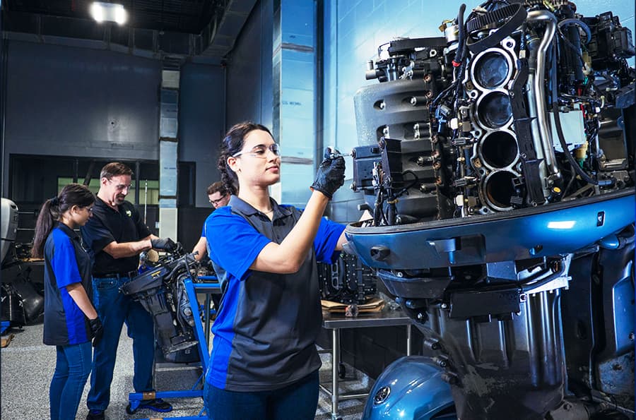 J-Tech Marine & RV Technology student working on a boat engine, using a socket wrench to remove a bolt.