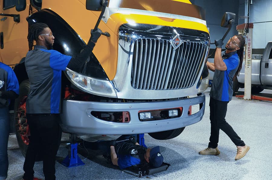 J-Tech Diesel Technology students working hands-on in the lab, opening up a semi truck's hood to work on its engine.