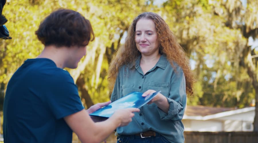 Mother sharing a brochure about dual enrolment at J-Tech with her son while he works on his old sports car.