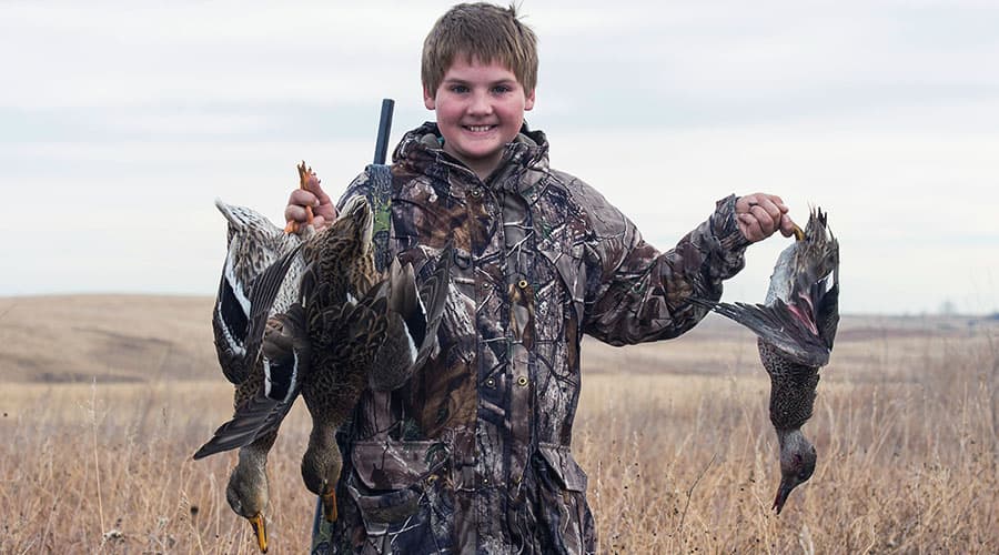 A young teenage boy hunting ducks and smiling.