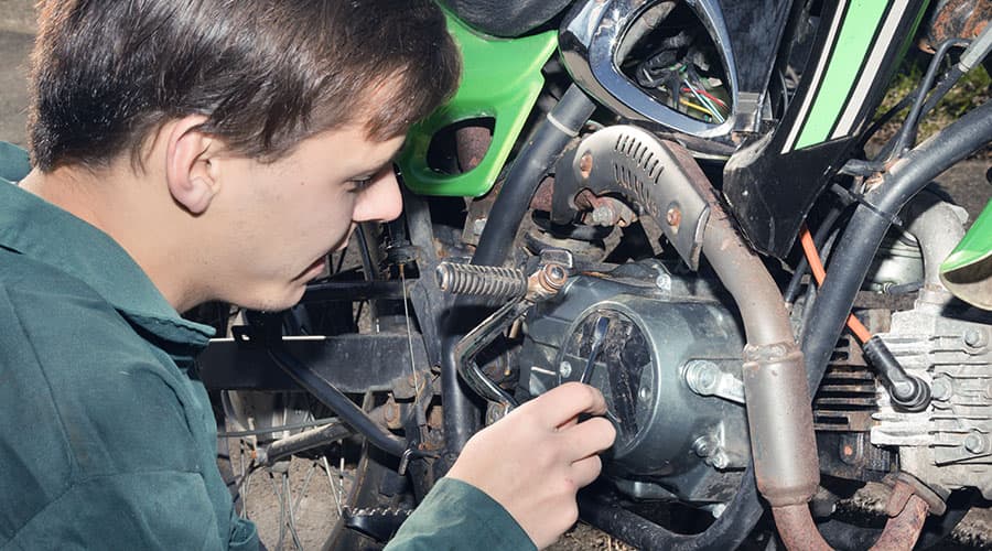 A teenage boy working on a dirt bike.