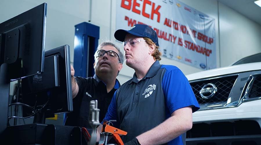 A J-Tech Automotive Technology student working alongside the instructor using a computer for car maintenance.